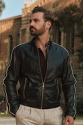 Man wearing a black leather jacket with white trim standing outdoors.