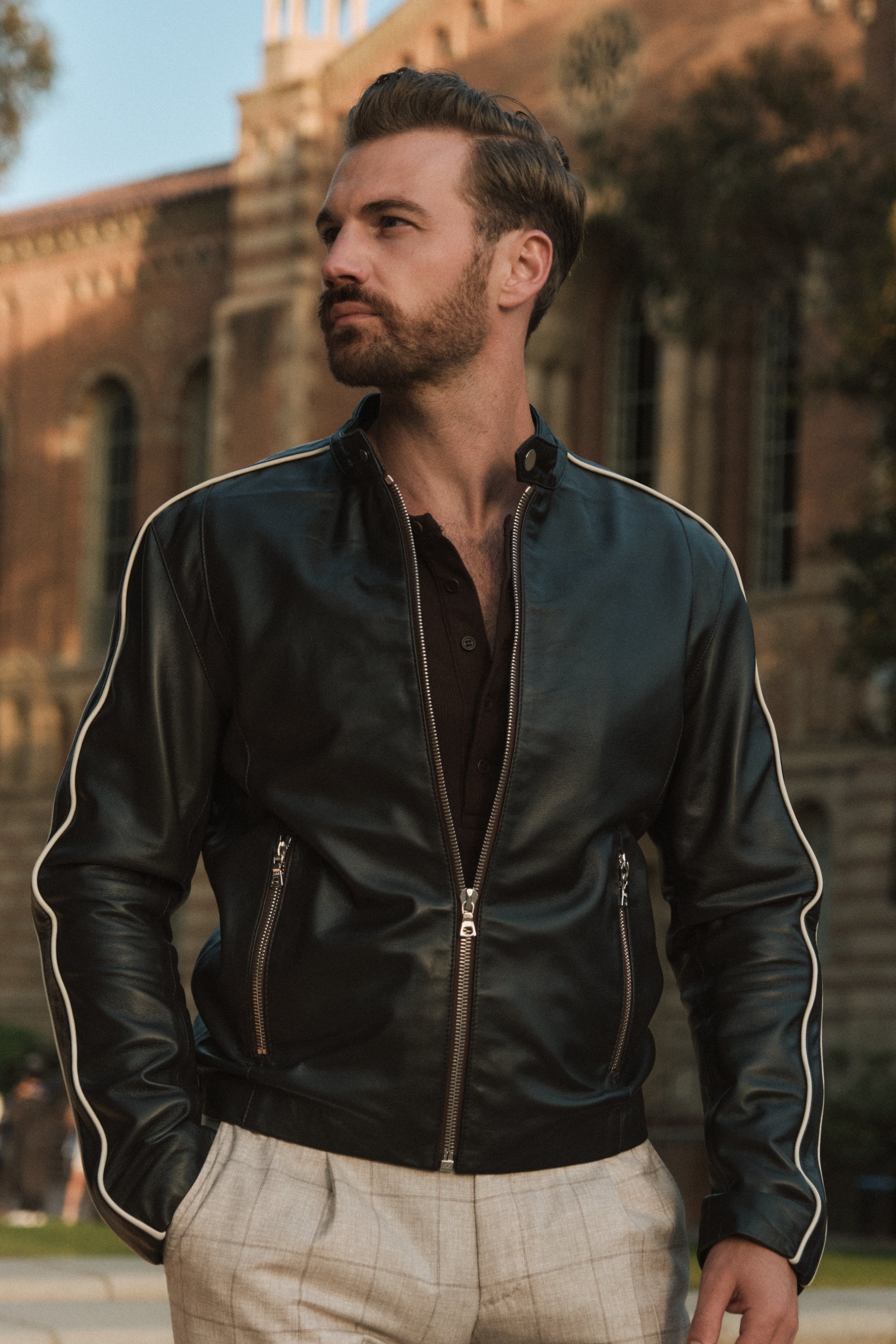 Man wearing a black leather jacket with white trim standing outdoors.