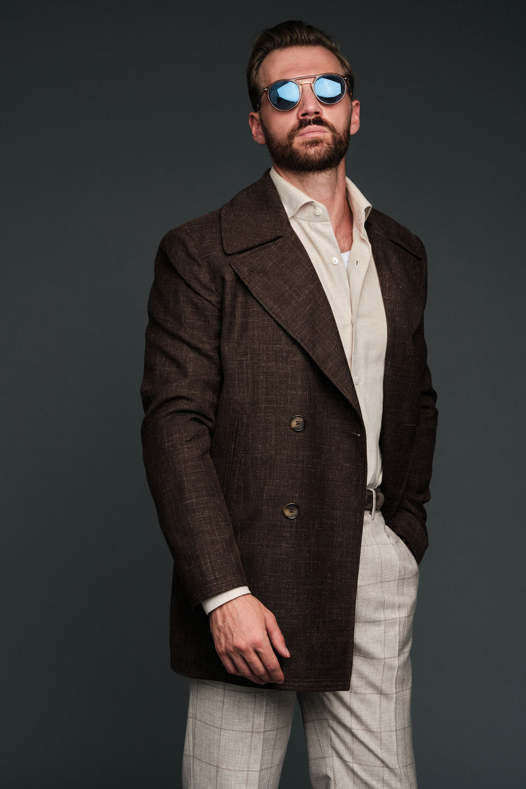 Man wearing a brown overcoat and sunglasses against a dark background