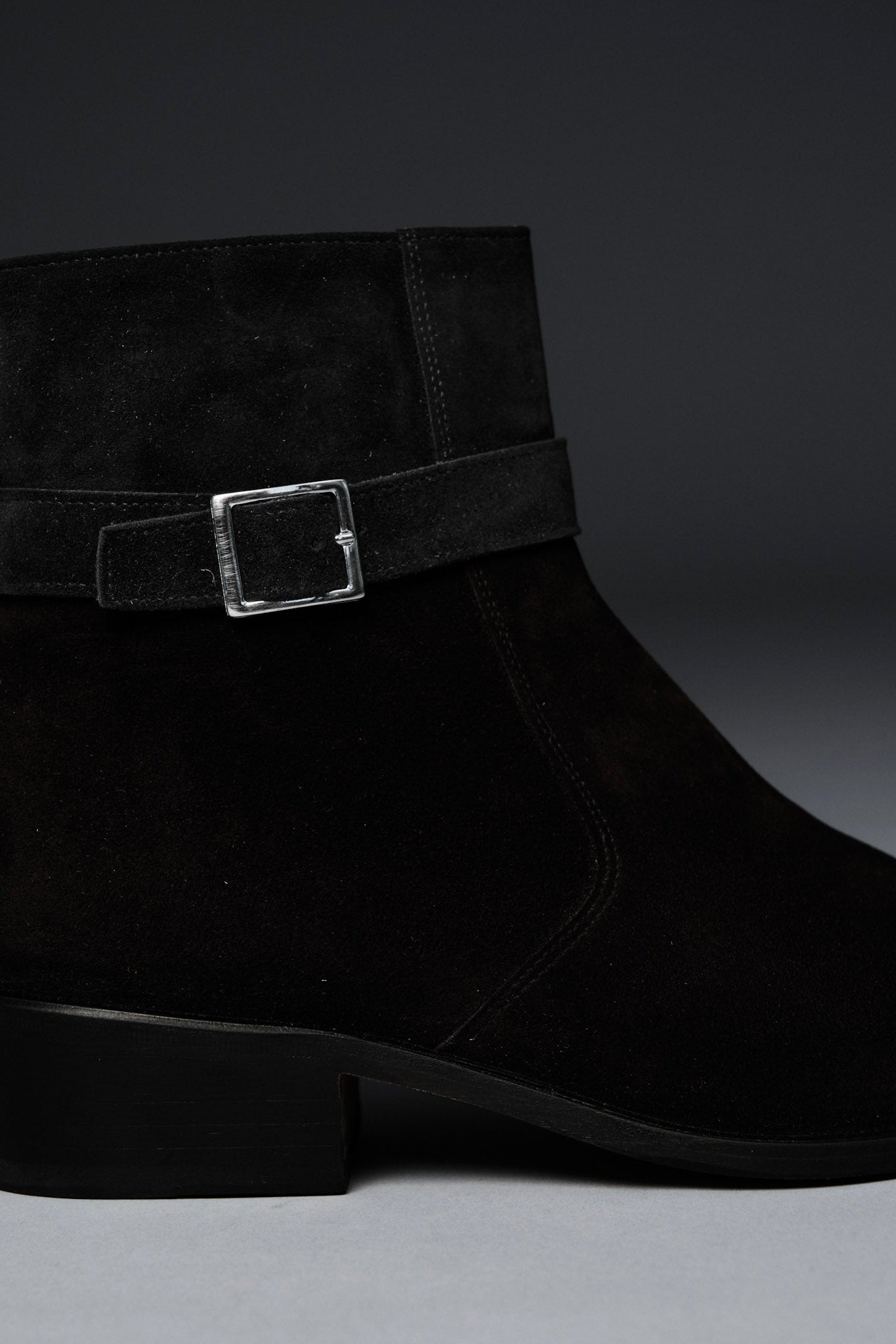 Black suede ankle boot with a buckle on a dark background