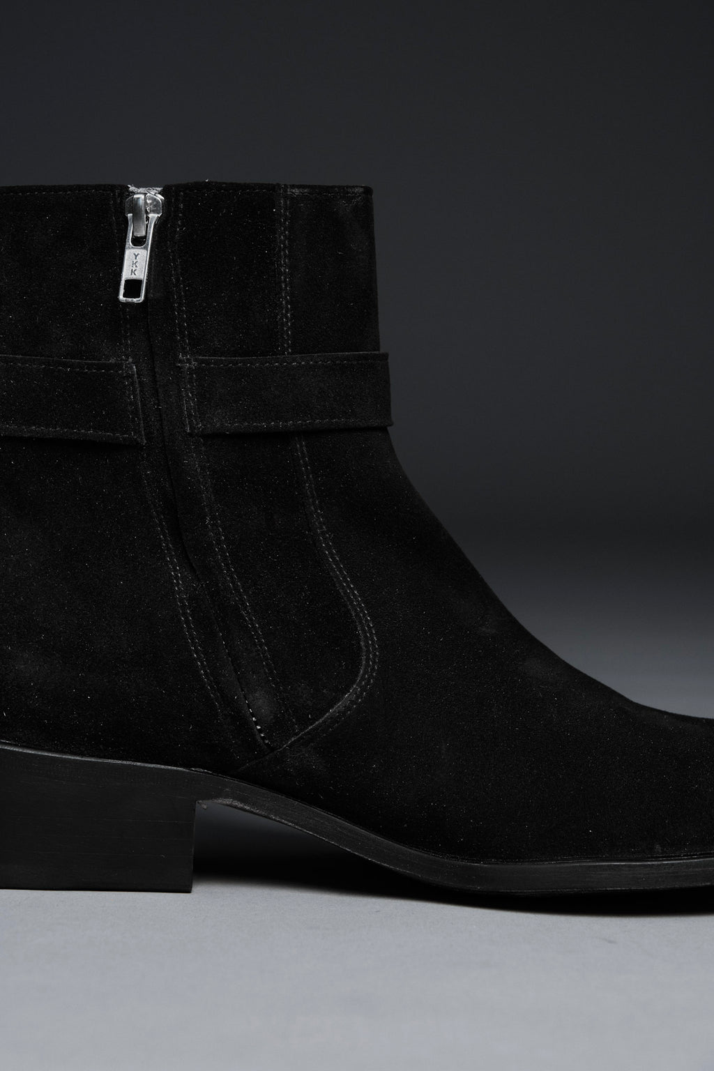 Black suede ankle boot with a zipper on a gray background