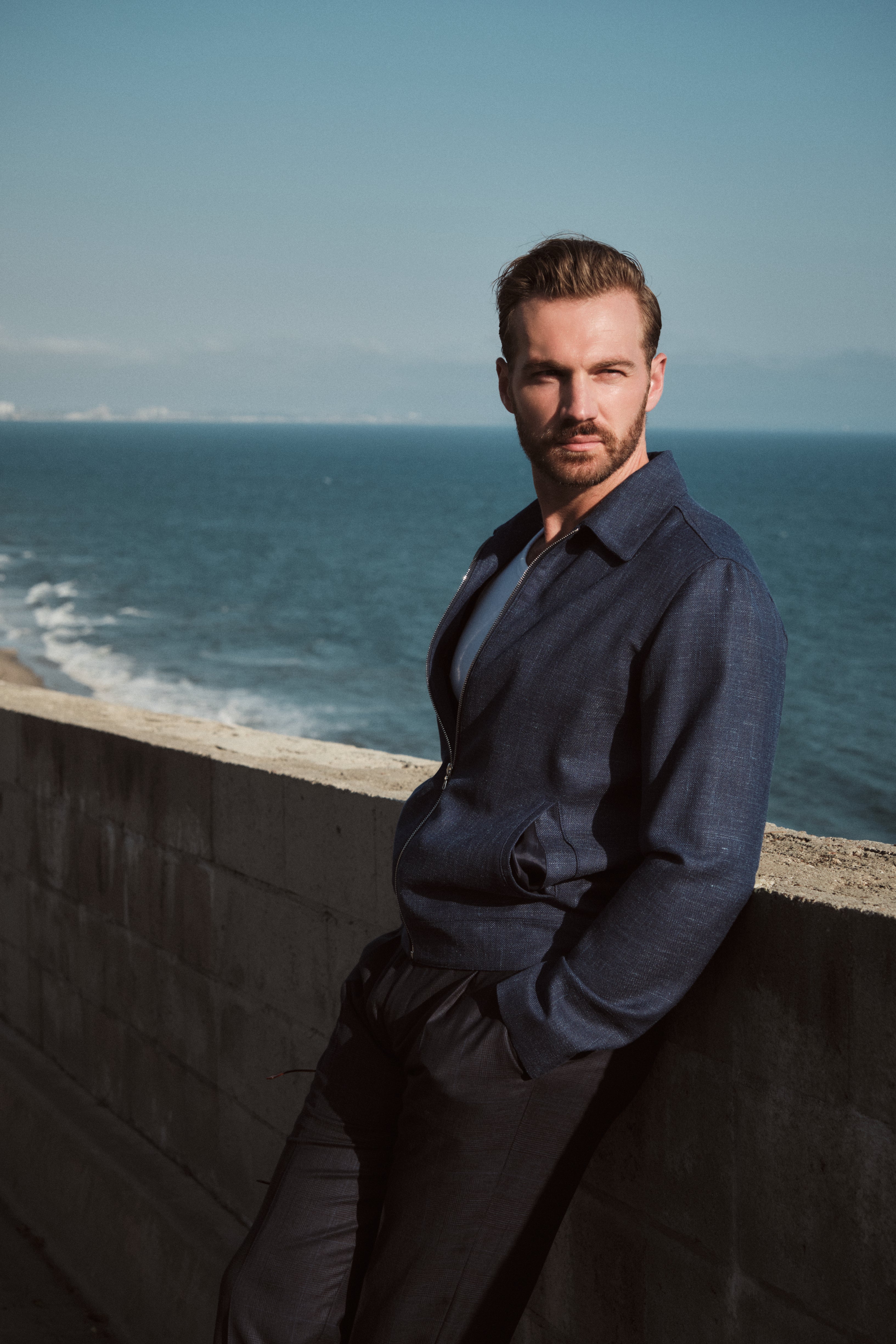 Man leaning against a wall with ocean and sky in the background