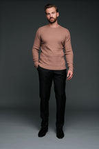 Man wearing a brown sweater and black pants against a dark background