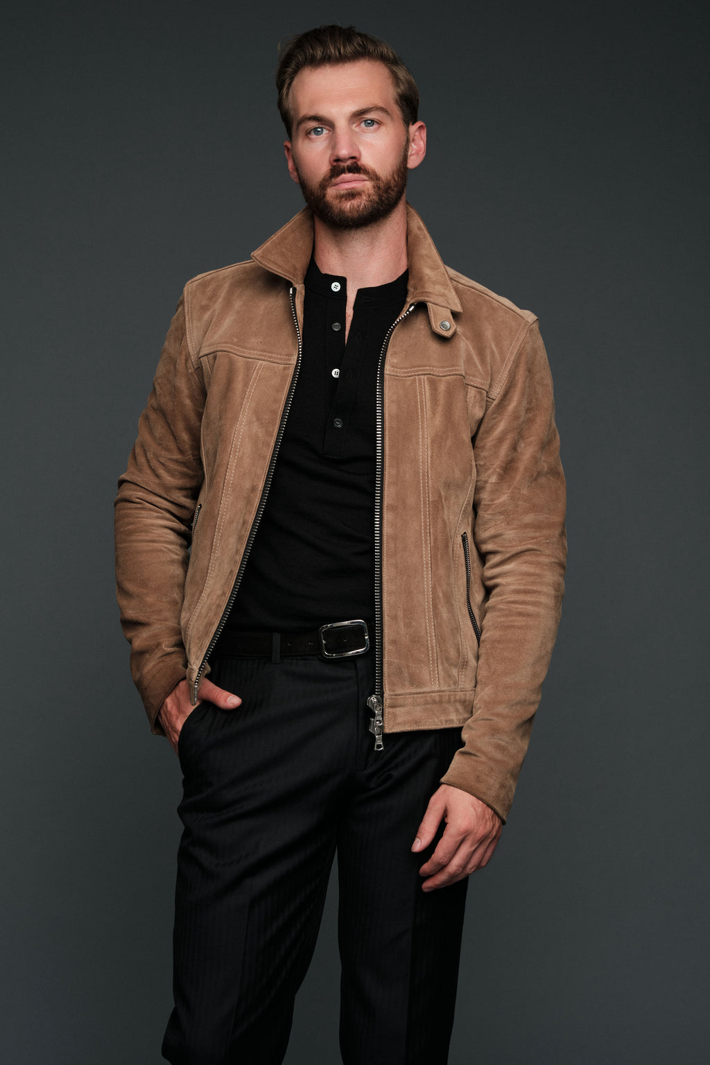 Man wearing a brown suede jacket over a black shirt on a dark background