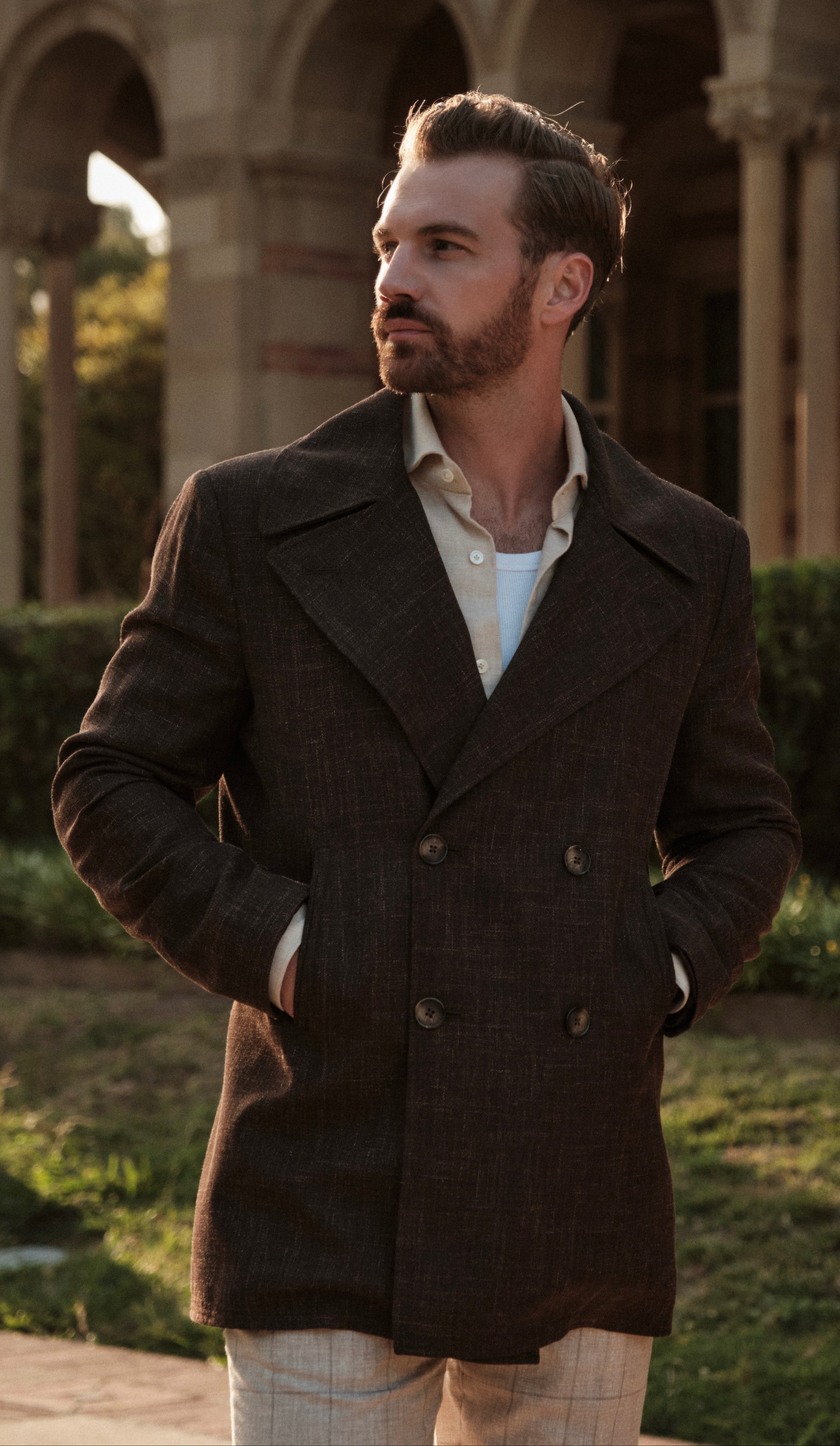Man wearing a dark coat standing in front of architectural arches