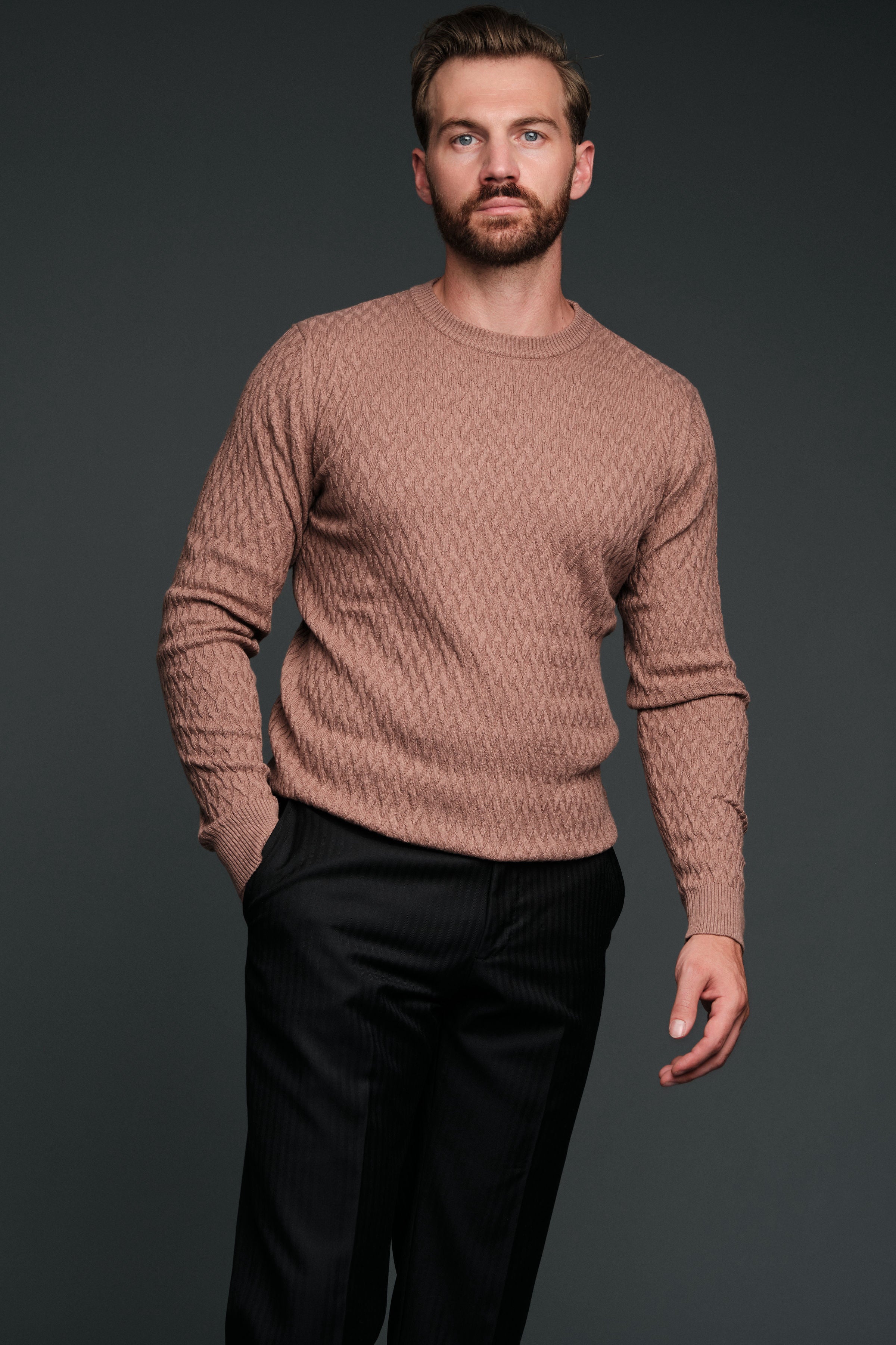 Man wearing a brown sweater and black pants against a dark background