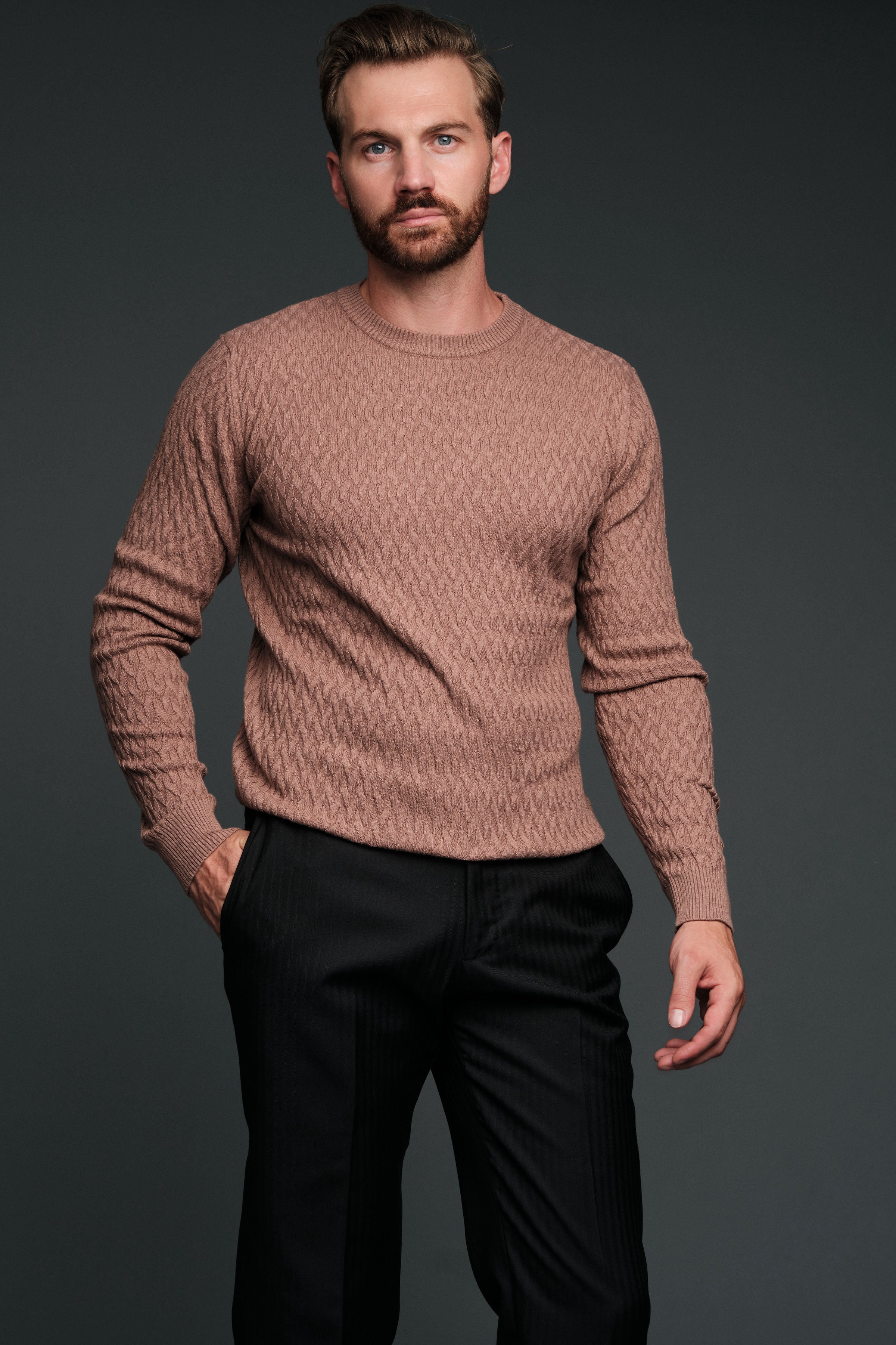 Man wearing a brown sweater and black pants against a dark background