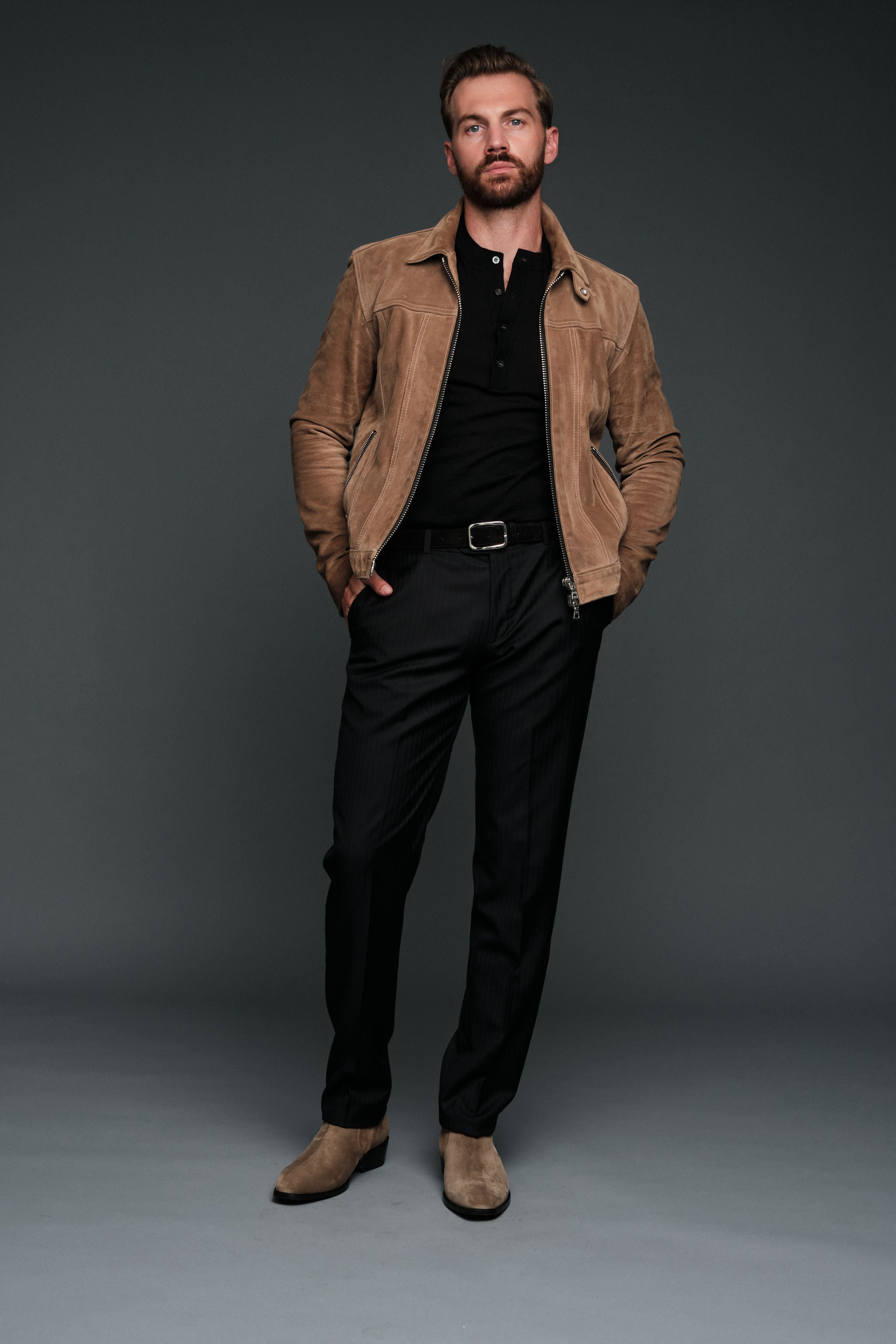 Man wearing a brown jacket over a black shirt and pants on a gray background