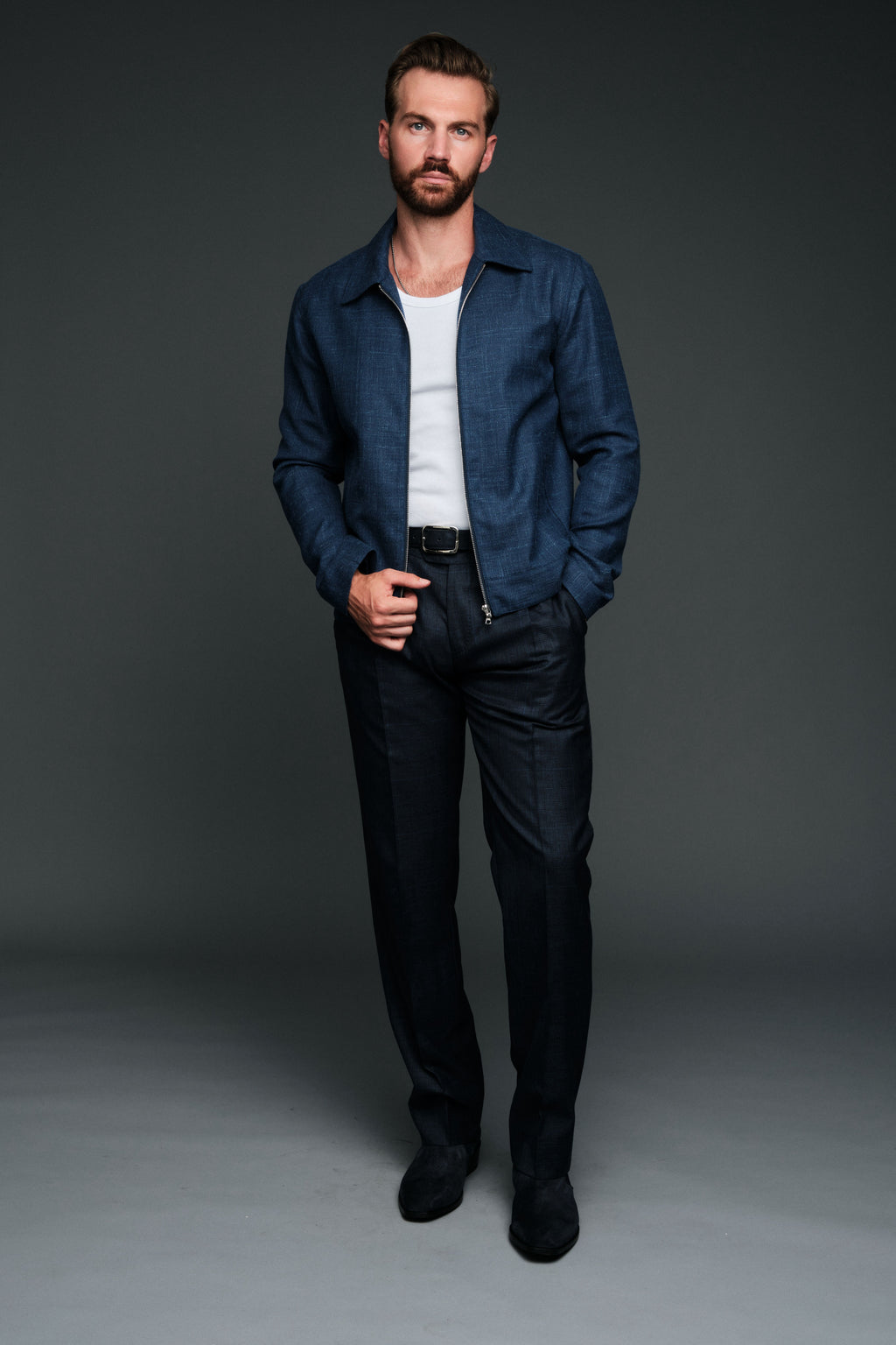 Man wearing a navy jacket, white shirt, and black pants against a gray background