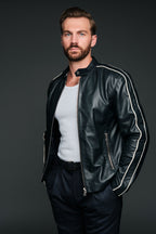 Man wearing a navy leather jacket with white stripes on a dark background