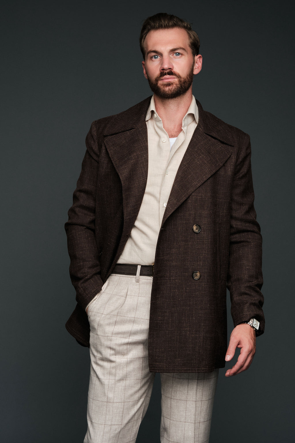 Man wearing a brown coat over a light shirt and pants on a dark background