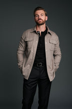 Man wearing a beige jacket over a black shirt and pants on a dark background