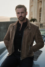 Man in a brown leather jacket sitting on a car with a building in the background