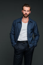 Man wearing a blue jacket over a white shirt and dark pants on a gray background