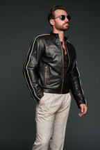 Man wearing a black brown leather jacket with white stripes and sunglasses on a dark background