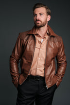 Man wearing a brown leather jacket over a beige shirt on a dark background