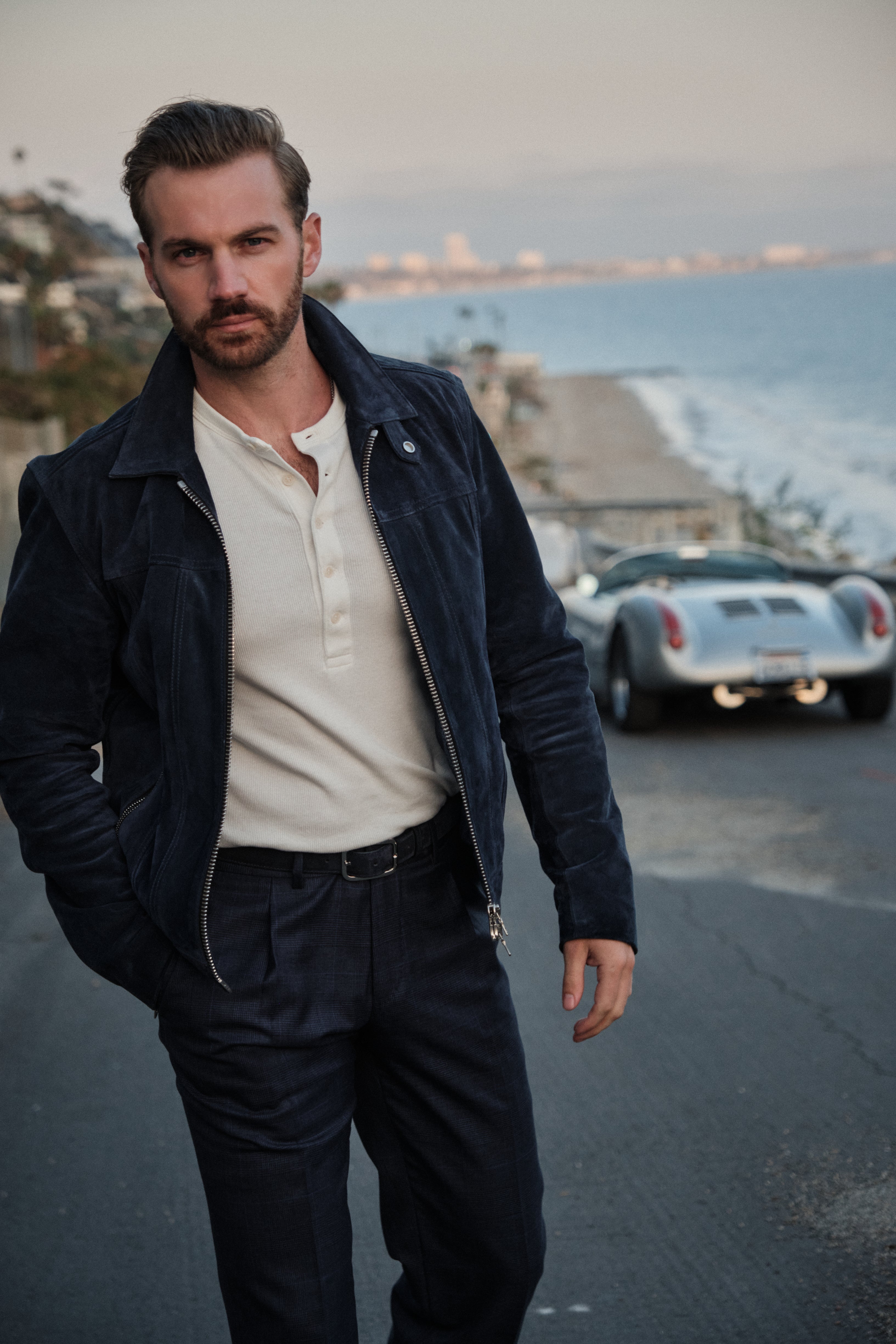 Man standing on a road by the sea with a car in the background