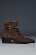 Brown suede boot with a buckle on a gray background