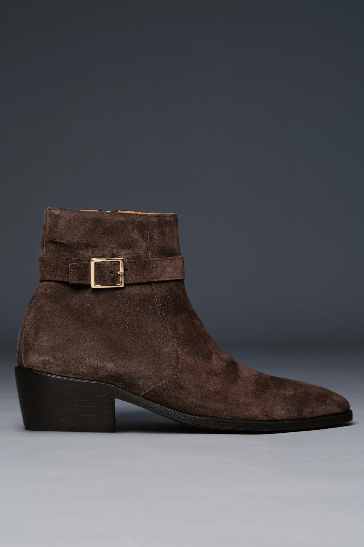 Brown suede boot with a buckle on a gray background