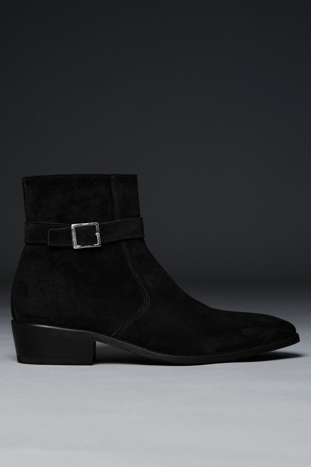 Black suede ankle boot with a buckle on a gray background