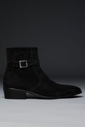 Black suede ankle boot with a buckle on a gray background