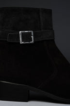 Black suede ankle boot with a silver buckle on a dark background