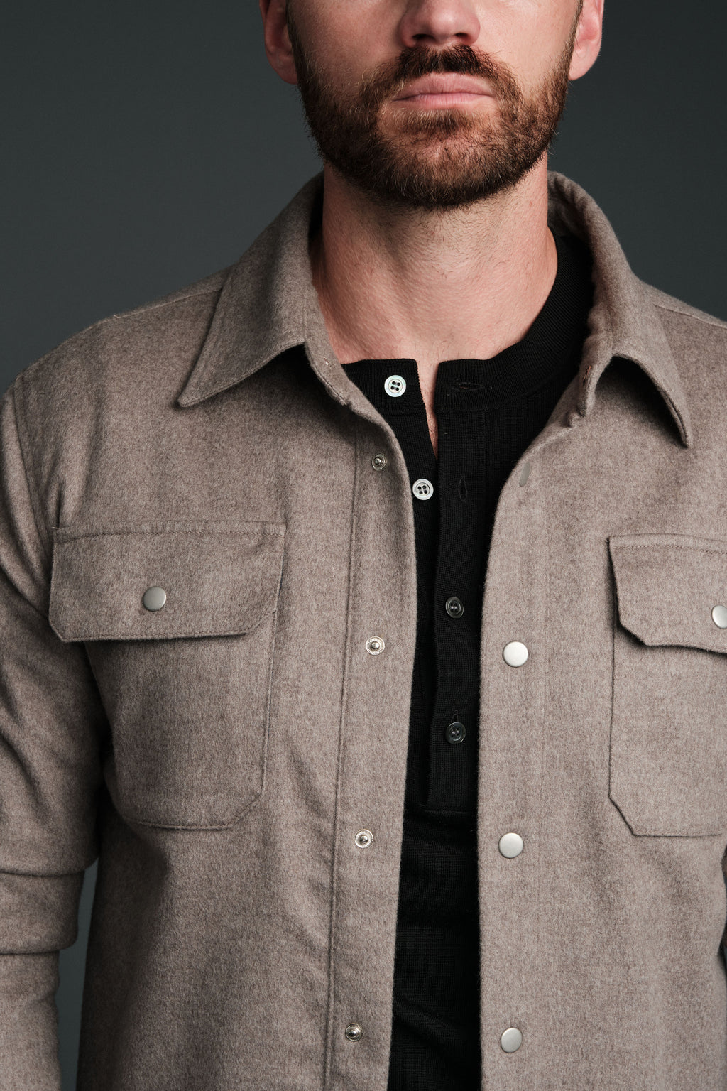 Man wearing a brown shirt with a black shirt underneath on a dark background