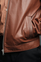 Close-up of a brown leather jacket with a zipper on a dark background