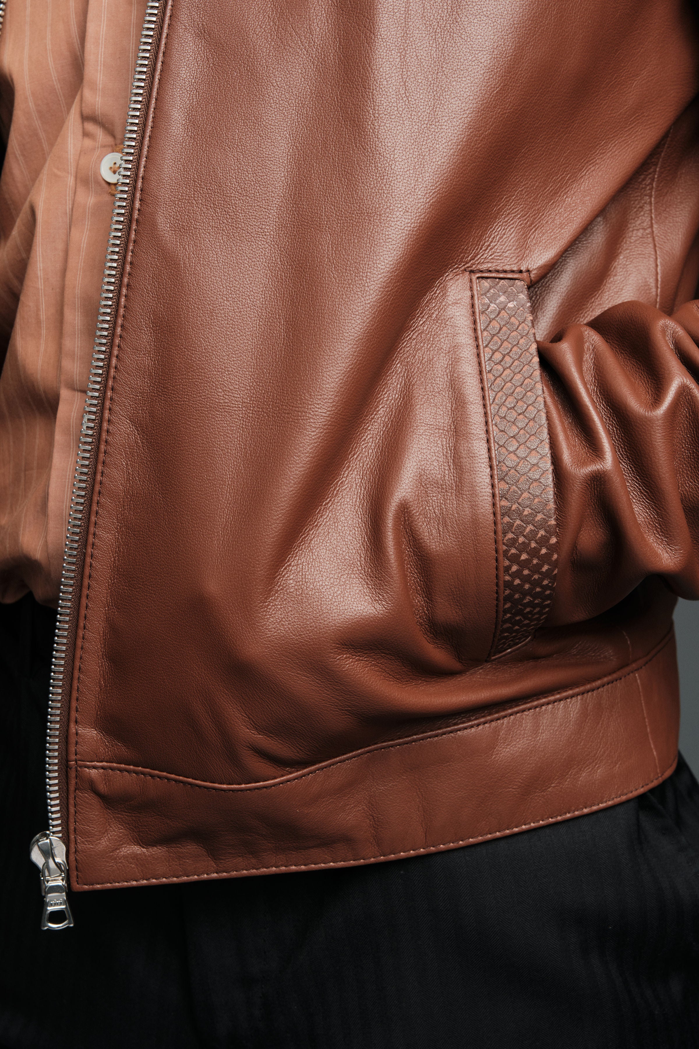 Close-up of a brown leather jacket with a zipper on a dark background