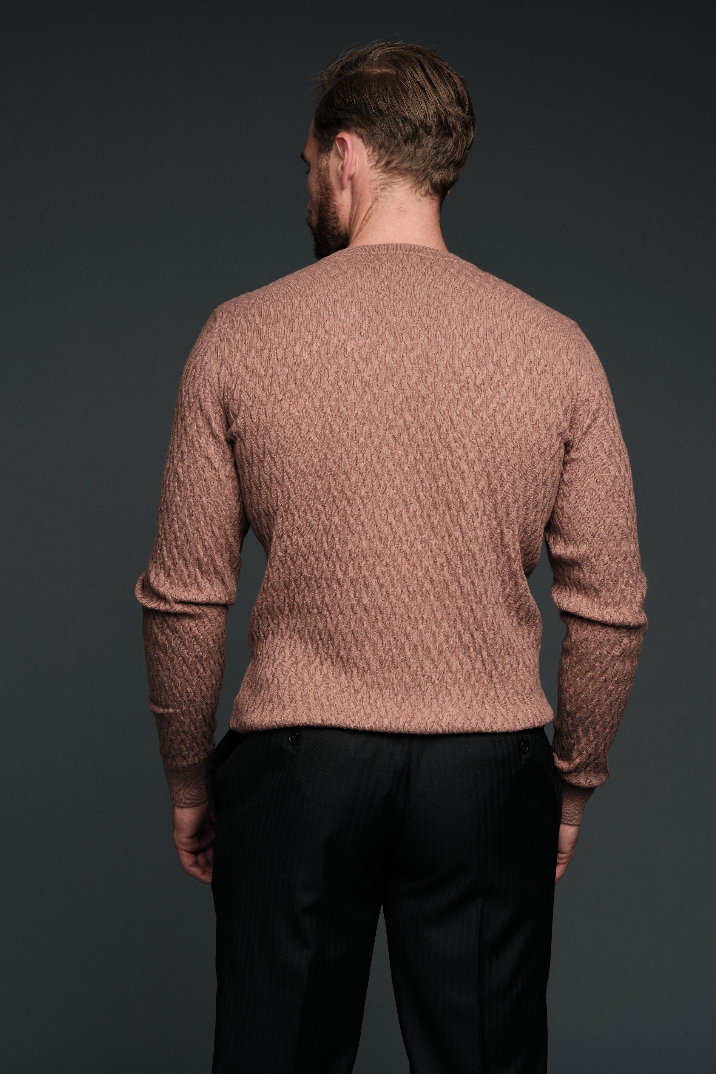 Man wearing a brown textured sweater and black pants against a dark background