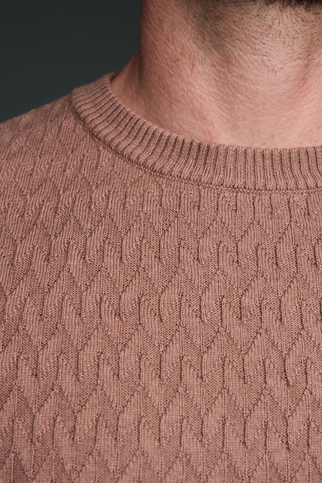 Close-up of a person wearing a brown cable knit sweater against a dark background