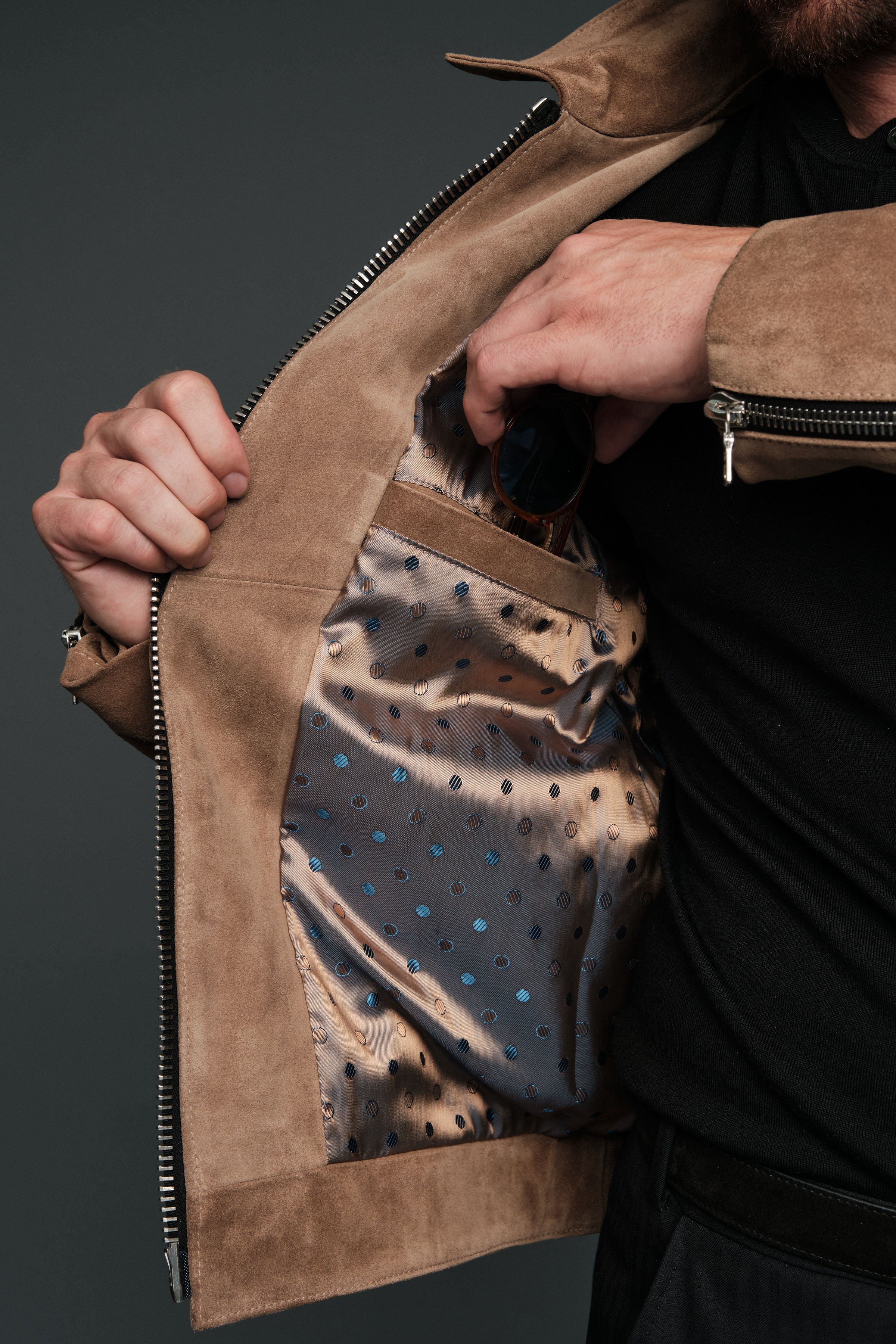 Person wearing a brown leather jacket with a patterned lining, on a dark background