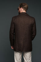 Man wearing a brown jacket and white pants against a dark background