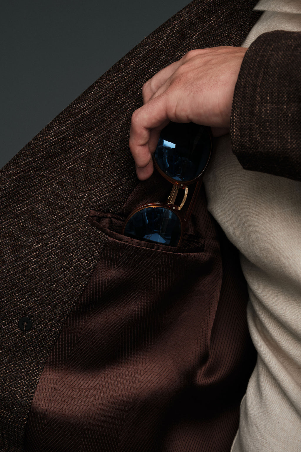 Hand reaching into a brown coat pocket to retrieve sunglasses.
