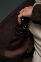 Hand reaching into a brown coat pocket to retrieve sunglasses.