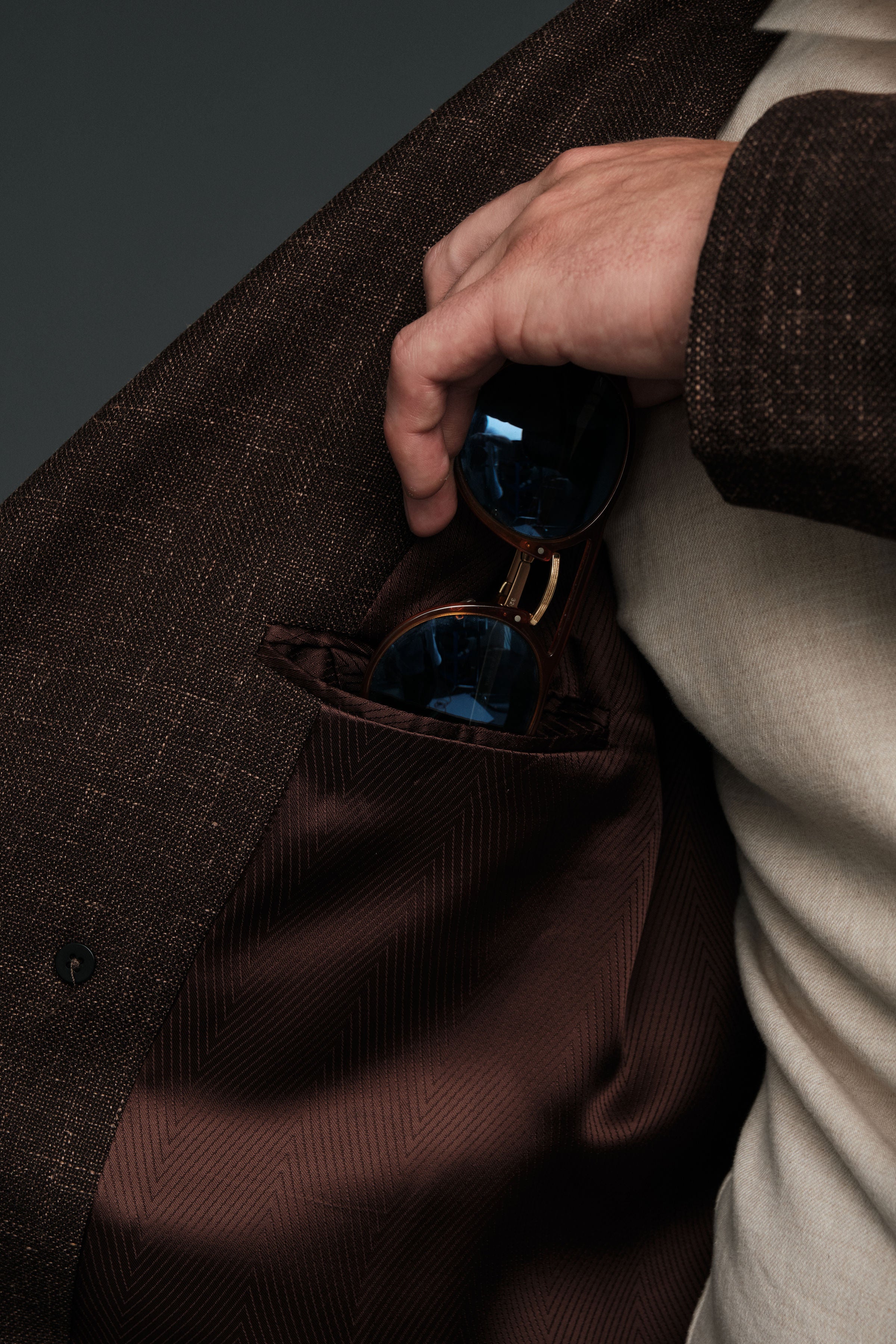 Hand reaching into a brown coat pocket to retrieve sunglasses.