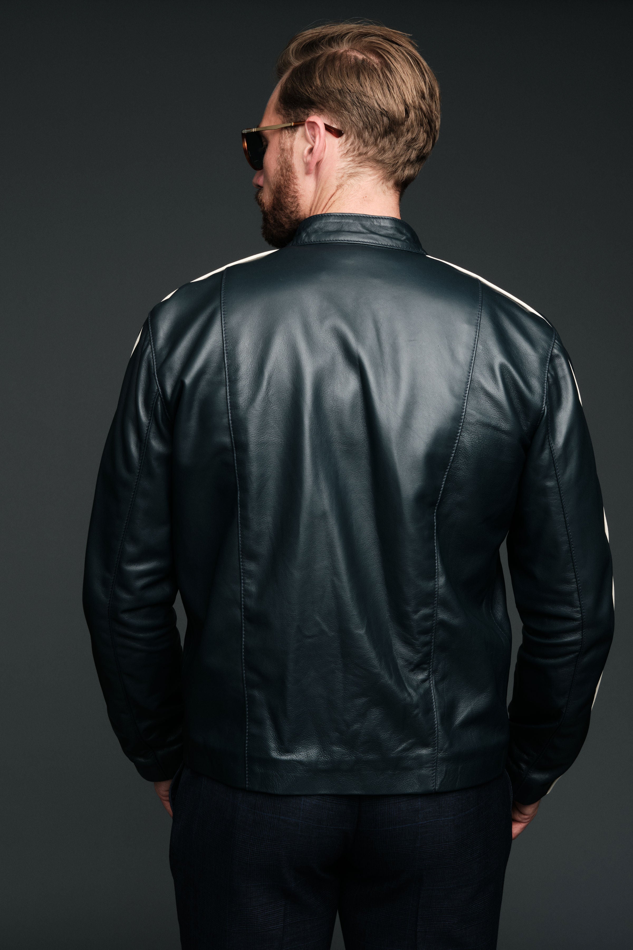 Man wearing a navy leather jacket with white stripes on a dark background