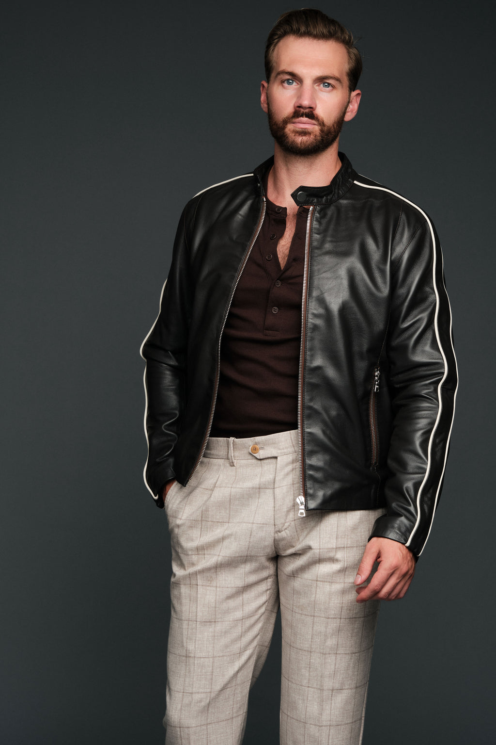 Man wearing a brown leather jacket with white stripes on a dark background