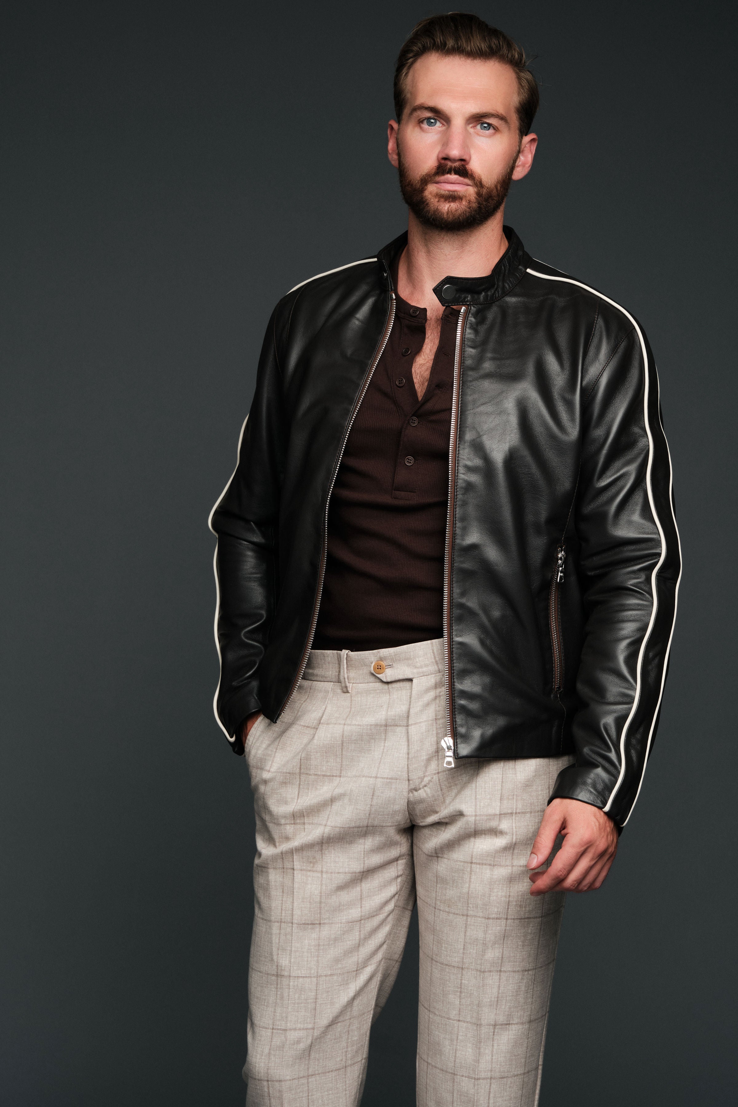 Man wearing a brown leather jacket with white stripes on a dark background