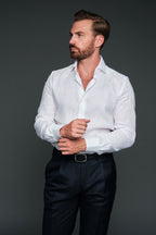 Man wearing a white shirt and dark pants against a gray background